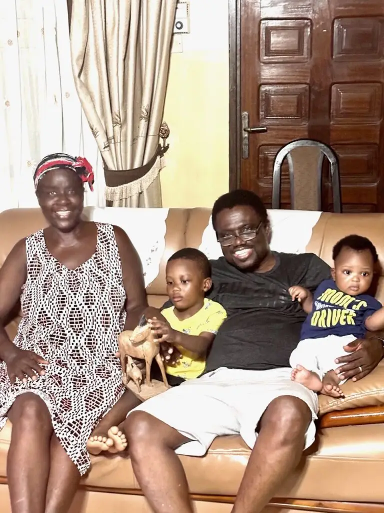 a smiling man and woman on a couch with the man carrying two cute kids